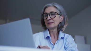Ofiste dizüstü bilgisayarda çalışan kıdemli bir kadın durup düşünüyor, ilham veriyor.