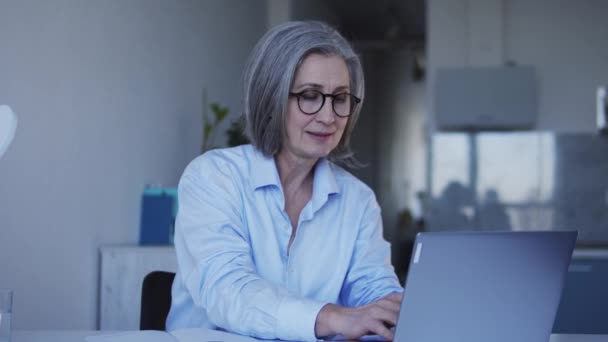 高级商业女性穿着时髦的眼镜和衬衫在自家办公室的笔记本电脑上工作 在笔记本上写下计划和任务 规划开新公司的策略 — 图库视频影像