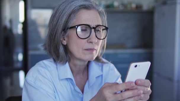 自宅のスマートフォンで働く眼鏡のシニア女性翻訳者 集中力の高さと顧客への責任感のために頭痛を感じる — ストック動画