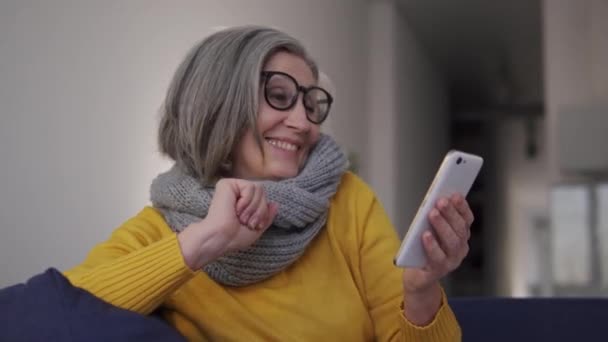 非常兴奋的女人 在智能手机应用程序上听最喜欢的音乐 坐在沙发上 在网上玩得开心 兴奋极了 — 图库视频影像