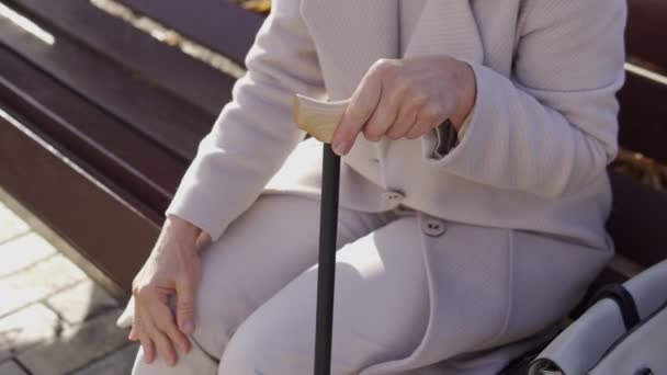 一个成熟的女人 拿着手杖坐在长椅上 揉揉着酸痛的膝盖 休息着 — 图库视频影像