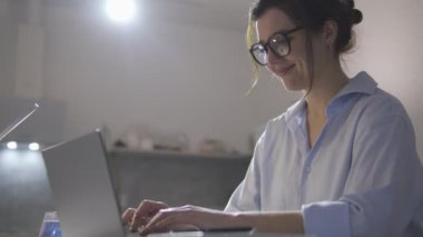Çekici bir kadın dizüstü bilgisayar yazarken gülümsüyor, sohbet ediyor ve sosyal ağlarda flört ediyor.