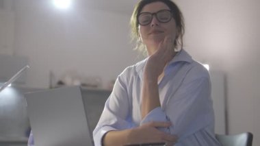 Heyecanlı kadın dizüstü bilgisayarını bitiriyor ve işyerinde oturup gülümsüyor.