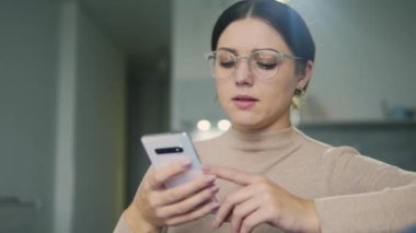 Büyük gözlüklü, üzgün kadın pazarlama müdürü sosyal ağ atölyesinde online siparişlerle ilgili sorunlar yaşıyor, sorun çözümünün ev telefonundan çalışmasını düşünüyor.