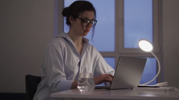 若い女性プログラマーは遅くまでオフィスでノートパソコンを使って仕事を楽しんで笑っています — ストック動画