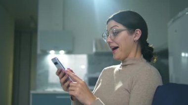 Mutlu olumlu kadın kanepeye oturup online oyunlar oynuyor, kumar oynuyor ve kumarhane uygulamasında kazanıyor, bedava dönüşler ve ekstra oyun parası kazanıyor.