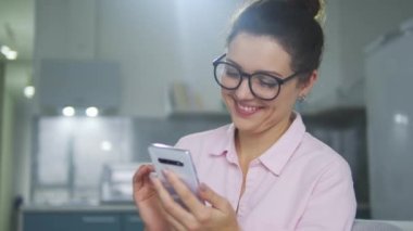 Gözlüklü güzel esmer kadın gülümsüyor, cep telefonunda yazıyor, flört uygulamalarında ya da habercilerde sohbet ediyor, seviniyor, sosyal ağlardaki yeni fotoğrafında beğenileri kontrol ediyor.