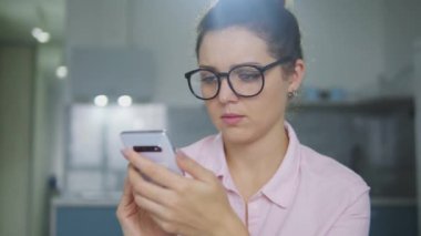 Saçı topuzlu kızgın bir kadın akıllı telefonuyla sorun yaşıyor, internet bağlantısı kötü, aramalar için bağlantı zayıf, uzaktan öğrenme ya da çalışma sorunları var.