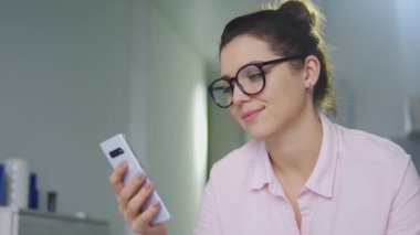 Şık gözlüklü ve şık gömlekli iş kadını samimi bir şekilde sevinç içinde, online olarak akıllı telefona bahis oynuyor ve para kazanıyor ve serbest dönüşler yapıyor, çevrimiçi piyango.
