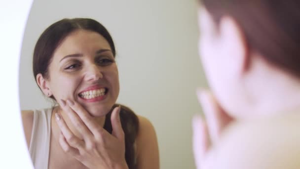 Молодая женщина смотрит в большое зеркало на зубы, у нее проблемы с зубами, стоматология — стоковое видео
