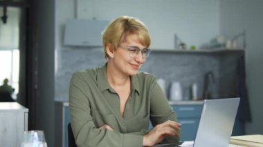 İş elbisesi ve gözlük takan son derece mutlu bir kadın web tasarımcısı dizüstü bilgisayardan geri bildirim alıyor, tasarım projesini satıyor, iyi bir iş teklifi alıyor.