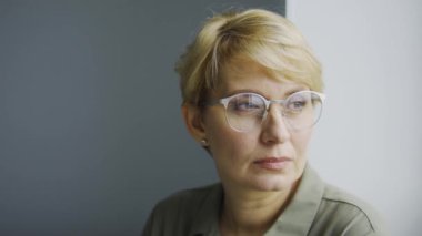 Düşünceli, gözlüklü, pencerenin kenarında oturan ve dışarı bakan, rutin işten bıkmış, ilham eksikliği, kadın hormonlarıyla ilgili sorunlar, avitaminoz veya depresyon