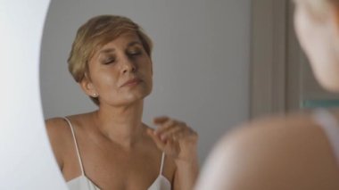 Güzel, şehvetli bir kadın zevk alıyor. Nazikçe yüzüne dokunuyor. Yaşlanma karşıtı kremle tatmin oluyor.