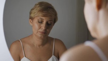 Şüpheci orta yaşlı kadın yeni bir krem deniyor yaşlanma ve kaldırma karşıtı, kaliteden ve etkinlikten şüphe duyan, yeni kozmetik üretim serisini test eden.