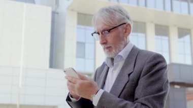 Gri saçlı adam akıllı telefon uygulaması üzerinden banka hesabını kontrol ediyor.