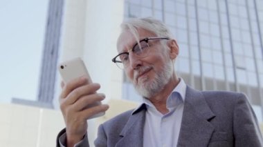 Gri saçlı adam akıllı telefondan mesaj okuyor ve gülümsüyor, iyi haberlerin tadını çıkarıyor.