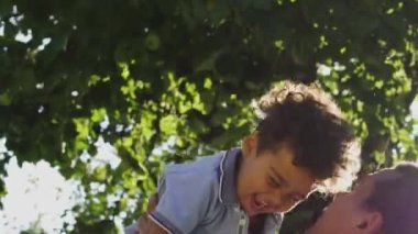 Çok ırklı bir baba küçük sevimli oğlunu gökyüzüne fırlatıyor ve ellerini tutuyor, çocuk gülüyor, aile birlikte eğleniyor, mutlu ve tasasız bir çocukluk geçiriyor, tatiller yapıyor.
