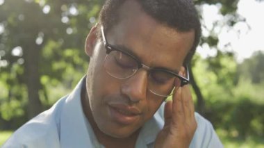 Gözlüklü, baş ağrısı ya da kulak ağrısı hisseden çift ırklı bir adam. Garip davranışlar.