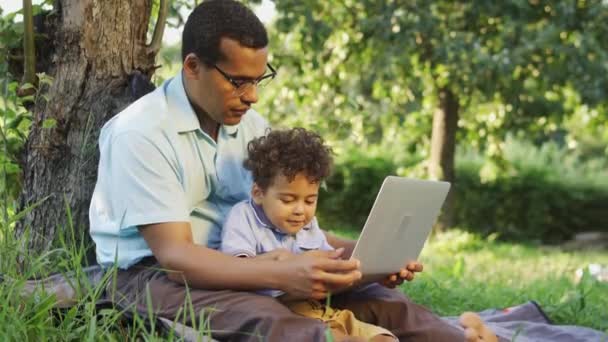 Uroczy Chłopiec Bawiący Się Laptopie Ojców Siedząc Trawie Pod Dużym — Wideo stockowe