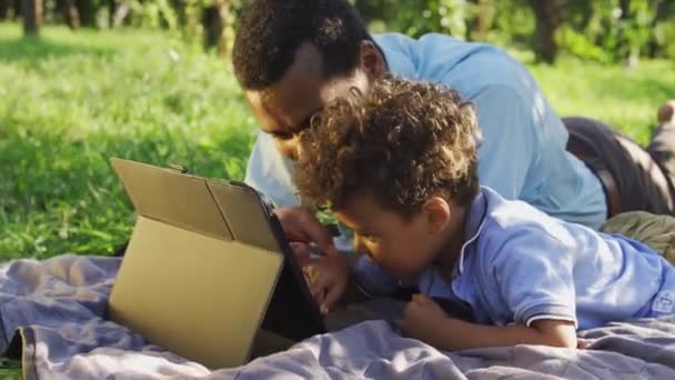 Çift Irklı Baba Oğul Dışarıda Battaniyeye Uzanmış Tablet Üzerinde Oyun — Stok video