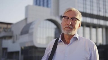 Otobüs durağının yanında duran çantalı gri saçlı adam tatile çıkıyor.