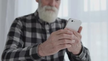 Yaşlı gri sakallı adam elinde akıllı telefon, çevirme numarası, internet uygulaması.