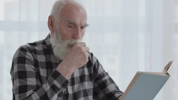 老人は拳で口を閉じて咳をし 部屋で本を読み 肺感染症 — ストック動画