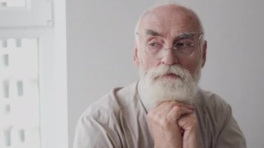 Elleri bağlı oturan, hayatı ve anıları düşünen düşünceli yaşlı bir adam.