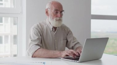 70 'li yaşlarda ciddi bir adam laptopta daktilo yazarak yıllık raporunu hazırlıyor.