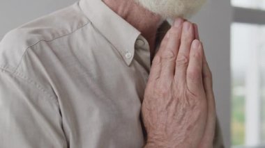 Gözlüklü yaşlı gri saçlı adam, dua ediyor, gözleri kapıyor, el ele tutuşuyor.