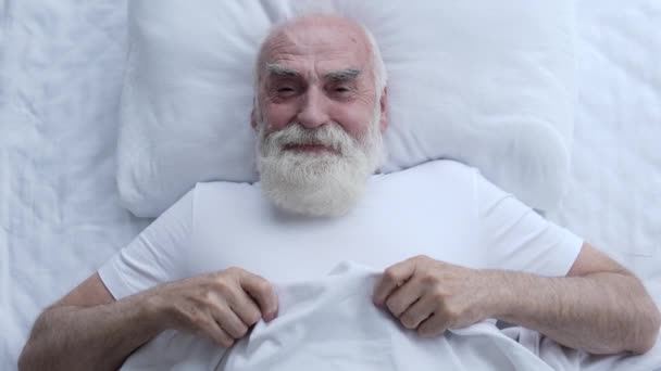 陽気な白髪の男がベッドに横になり 幸せな気分で 面白い瞬間を考えて — ストック動画