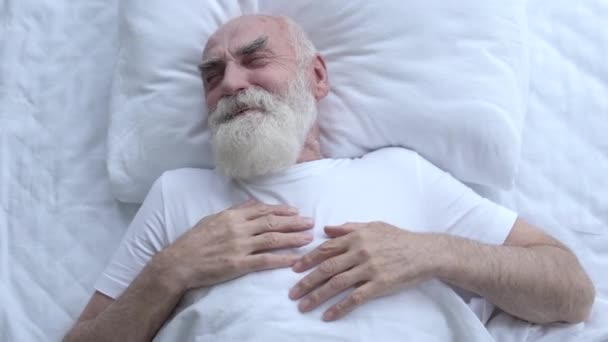 ハンサムな成熟した年金受給者は笑い ベッドでリラックスし 幸せな瞬間を覚えている — ストック動画