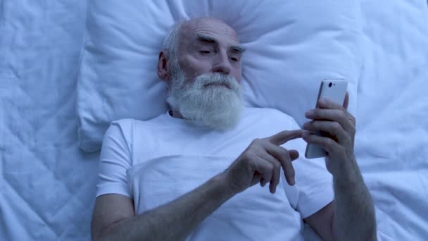 現代人は夜にベッドに横たわって スマートフォン上でソーシャルネットワークアプリをスクロールします — ストック動画