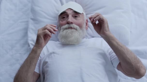 満足した老人は 睡眠の目のマスク ライトブロック 就寝時のルーチンを置く — ストック動画