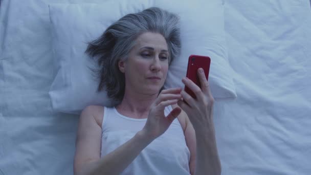 笑顔の女性は スマートフォンで写真をスクロールします 夜にベッドに横たわって オンライン — ストック動画