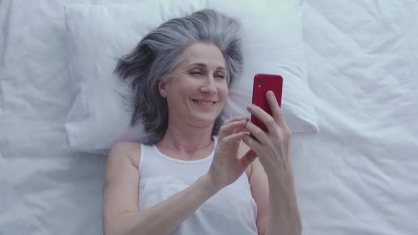 幸せな女性笑い スマートフォンで面白いビデオを見て ベッドでリラックス ガジェット — ストック動画