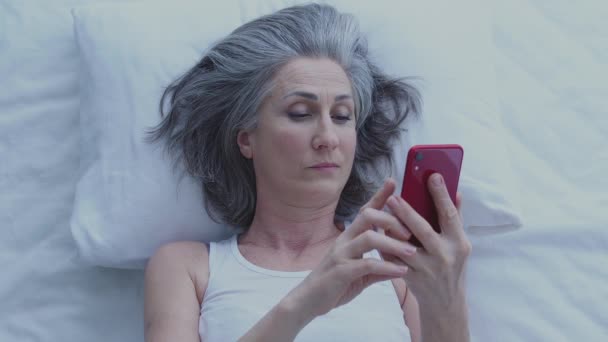 ベッドに横たわっ スマートフォン上で写真をスクロールする退屈Yawning女性 — ストック動画