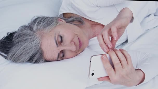Starší Usměvavá Žena Kontroluje Oznámení Telefonu Čte Zprávy Ležící Postel — Stock video