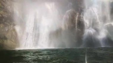 Suyun içindeki gri-kahverengi granit kayalar arasında bir şelalenin yavaş çekim sahnesi, su yüzeyi alt ön planda vahşice dans ediyor ve tüm olay yerinde vahşi su püskürtüyor, kamera şelale boyunca yukarı doğru hareket ediyor.