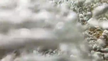 Yavaşça yakın çekim, temiz bir su akıntısının hafif bir düşüş içinde yüzeye doğru hareket eden kamera ve dans eden baloncuklar ile bir havuza düşüşü.