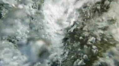 Yavaş çekim, temiz bir su akışının hafif bir düşüş içinde yüzey altında yavaşça hareket eden kamerayla ve küçük girdaplarda dans eden baloncuklarla bir havuza yakın çekimi.