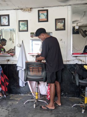 Şık üniformalı profesyonel berberler ve müşterilerinin saç kesimleri. Sandalyedeki küçük çocuk ve çizgili saç kesimli kırmızı bir elbise giyiyor. Modern berber dükkanı..