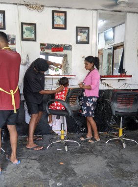 Şık üniformalı profesyonel berberler ve müşterilerinin saç kesimleri. Sandalyedeki küçük çocuk ve çizgili saç kesimli kırmızı bir elbise giyiyor. Modern berber dükkanı..