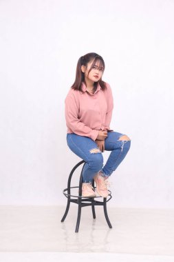 Güzel, siyah saçlı, 20 'li yaşlarda, basit bir pembe tişört giyen, gülümseyen, stüdyo resminin solundaki sandalyede oturan, hizmet terfisi için beyaz arka planda oturan bir kadın.