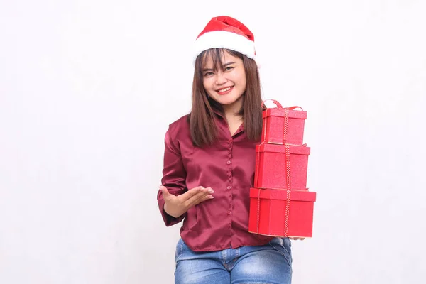 Beautiful young Southeast Asian girl surprised bringing 3 boxes of gifts at Christmas wearing Santa Claus hat modern red shirt outfit introducing boxes all white background for promotion and advertising