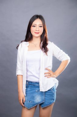 Sol belini içeride tutarken kameranın önünde poz veren zarif Asyalı kadın. Moda promosyonu kadın gömlek fotoğraf seansı gri arka plan stüdyosunda