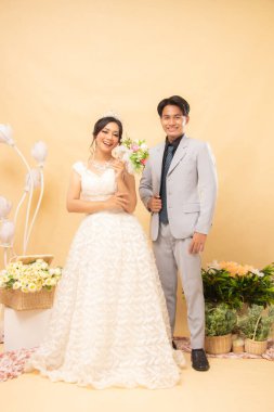 Kadın ve erkek resmi pozlarda neşeli bir yüz ifadesi. Rahatça durup gülümsüyorlar. Kapalı alanda fotoğraf çektirmek için sabırsızlanıyorlar. Evlilik Ulusal Gelin Stüdyosu