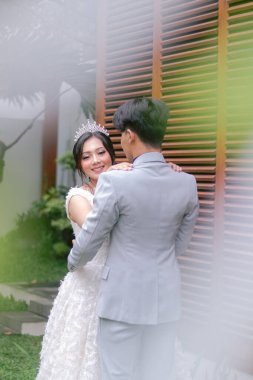 Zarif pozlar veren bir çift kadın ve bir erkek fotoğraf çekiminde kameraya bakan bir kadının karşısında dururlar. Ulusal Gelin Açık havada düğün çifti