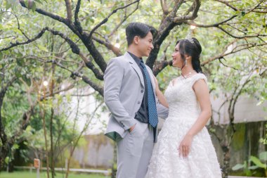 Bir çift erkek ve kadın, zarif bir şekilde karşılarında duran bir adama romantik ve samimi bir şekilde parktaki fotoğraf çekiminde güzel elbiseler giymiş bir kadına bakıyorlar. Ulusal Gelin Açık havada düğün çifti