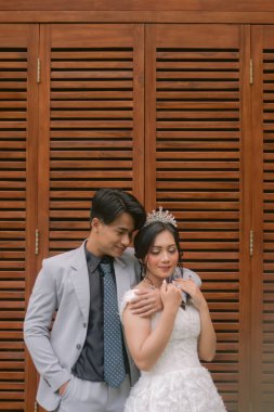 Zarif pozlar veren bir çift kadın ve erkek kollarını arkadan sarıp parktaki bir fotoğrafta güzel elbiseler giyip gözlerini yan tarafa kapatıyorlar.